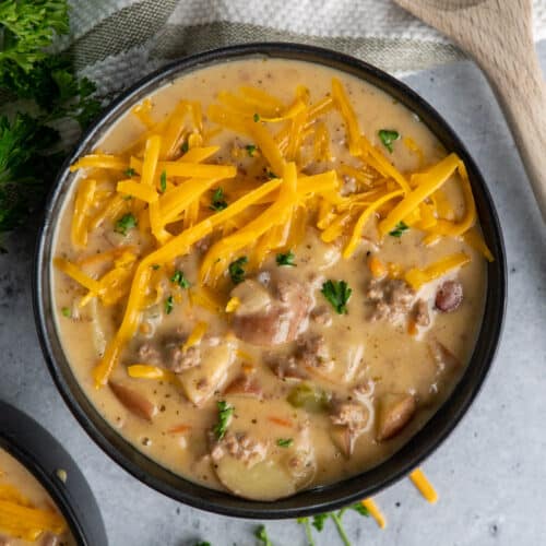 The Best Cheeseburger soup in a black bowl and garnished with cheddar cheese.