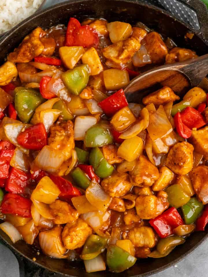 Sweet and sour chicken in a skillet with a wooden spoon.